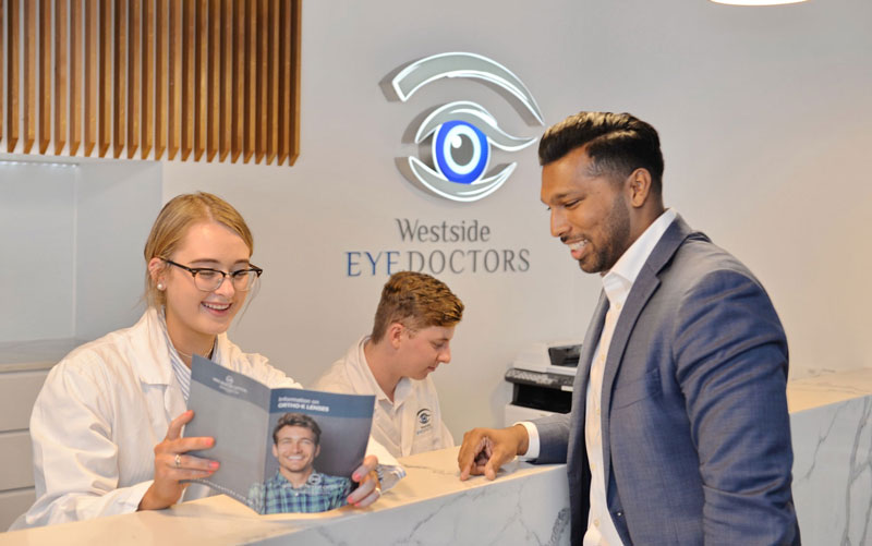 Reception staff at Westside Eye Doctors explaining lens options to a well dressed patient in a suit